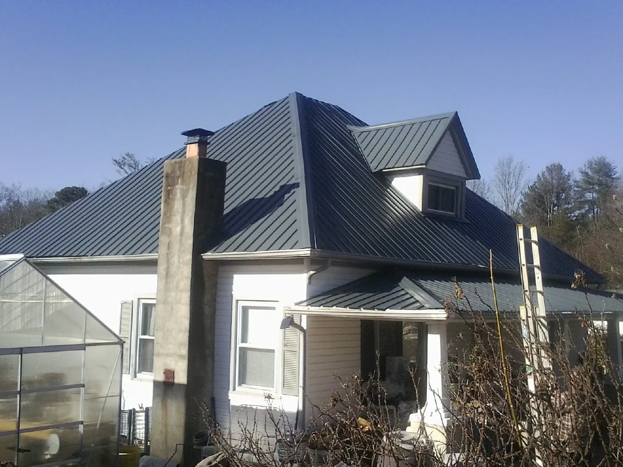 Dark blue standing seam metal roof on a white farmhouse with dormer — Slate & Tile Roof Repair by Roofing Brothers in Harvest