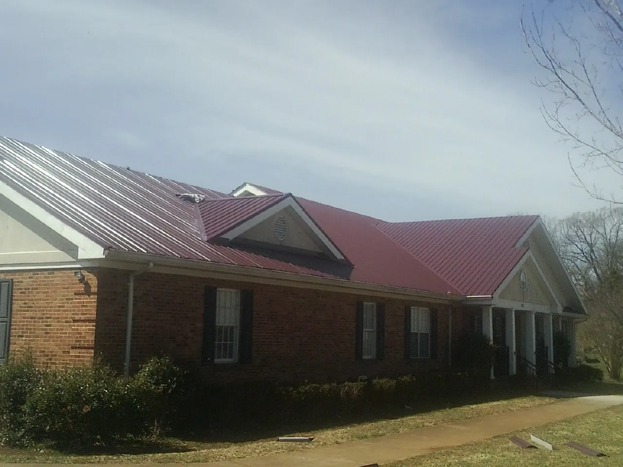 Red metal roof with gabled entries on a long brick building, from a Hail Damage Roof Repair job in Harvest
