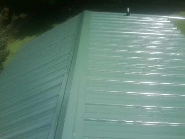 New green metal panels meeting at the ridge of a roof — Flat Roof Repair work by our crew in Harvest