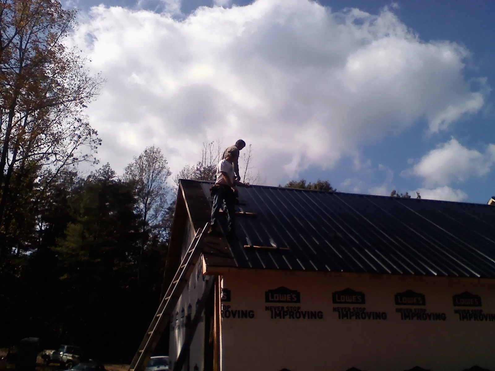 Roofer fastening dark metal panels high against a cloudy sky, from a Roof Inspection job in Harvest