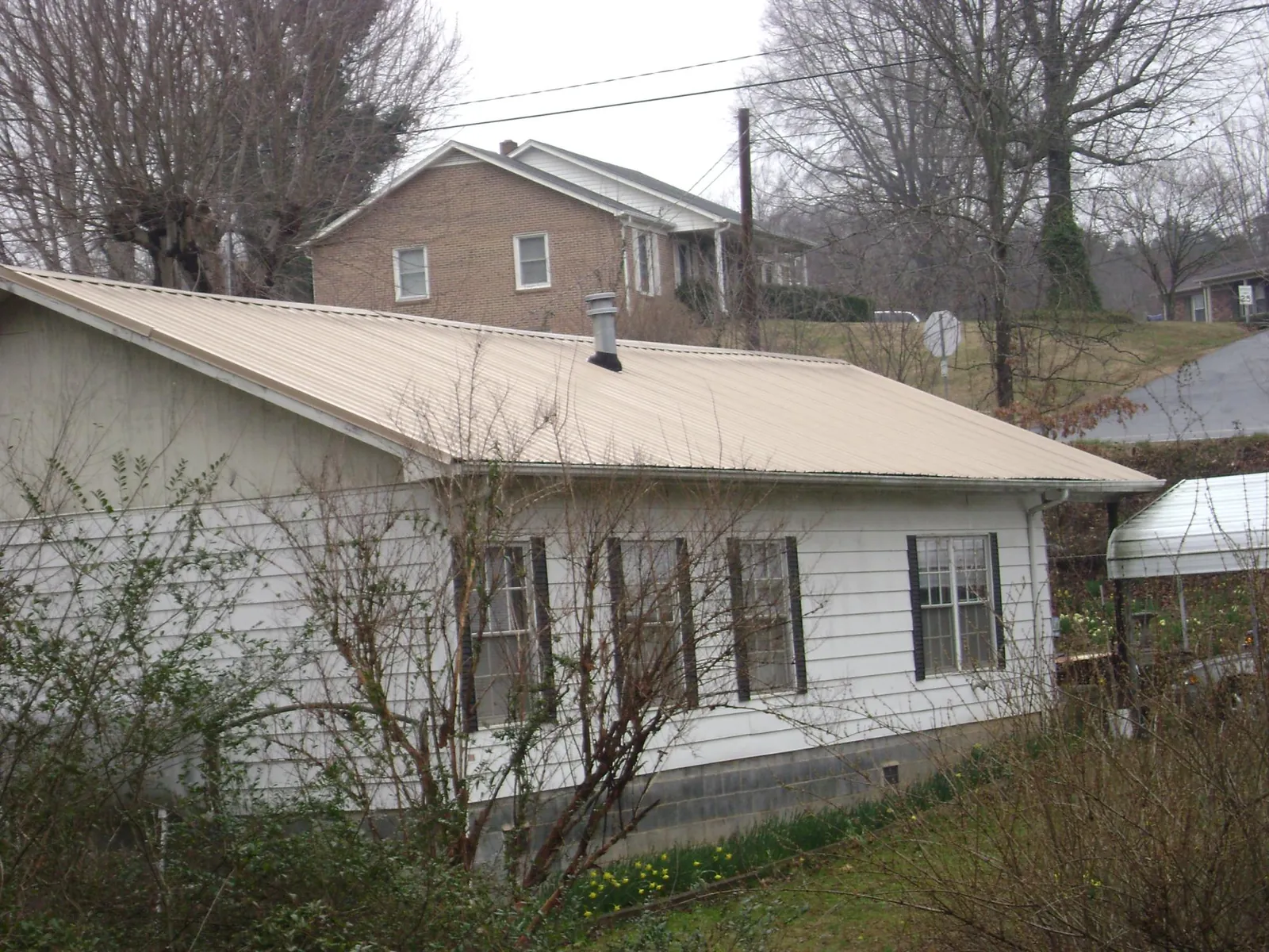 Tan metal roof on a white sided house set into a hillside — Commercial Roofing by Roofing Brothers in Harvest