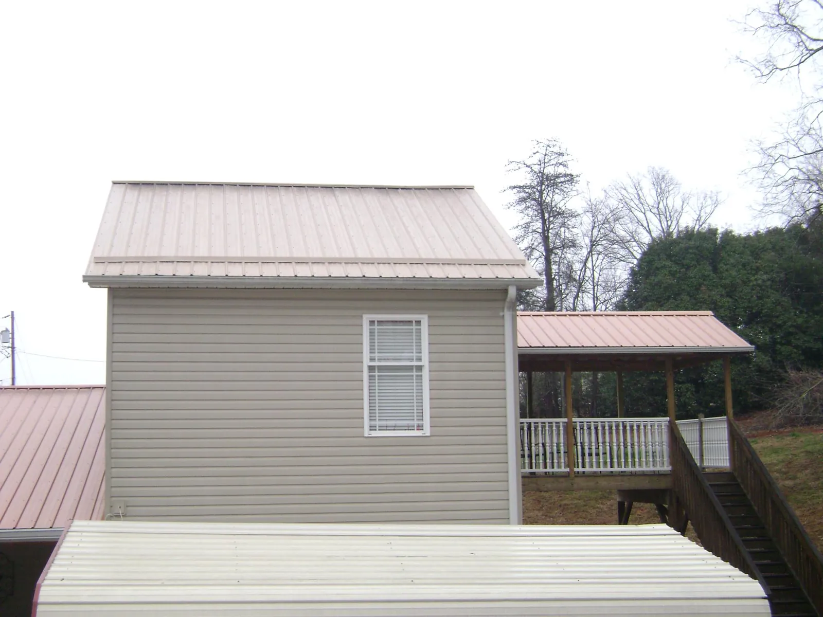 Tan metal roofs on a two story addition and attached porch, from a Roof Replacement job in Harvest